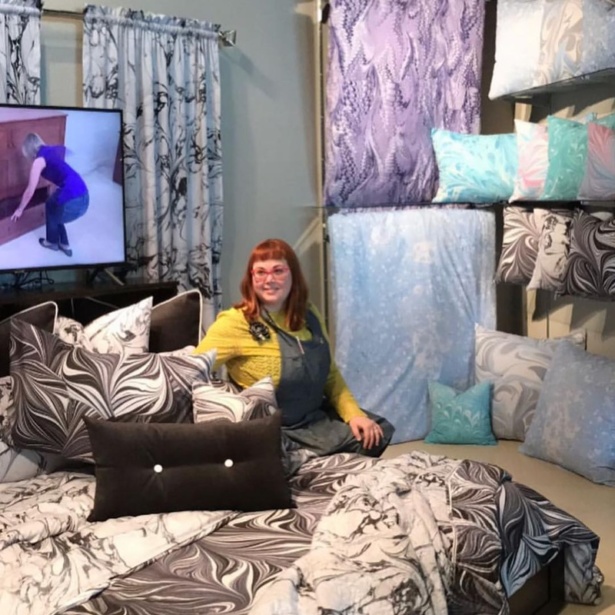 Surface designer Heather RJ Fletcher with her designs on bedding at Las Vegas Market, via her Instagram @theartofmarbling