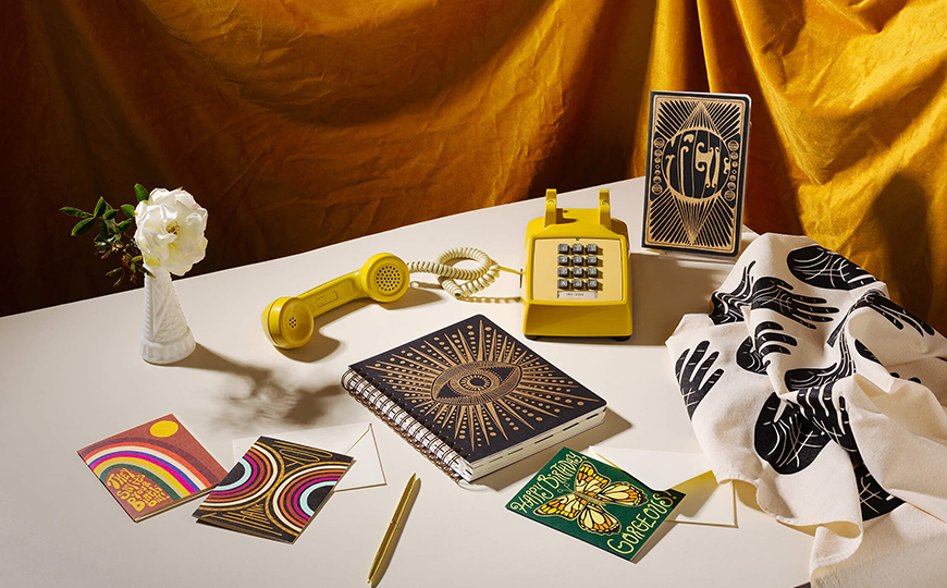 Product photography styled to capture the retro vibe. Shown here are greeting cards and a planner with bold, retro artwork. Vintage props set the mood. 